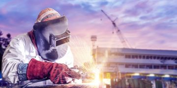 double exposure concept, worker arc welder piping welding buiding in shipyard background soft monotone